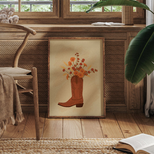 Framed artwork of a cowboy boot with flowers on a wooden floor.